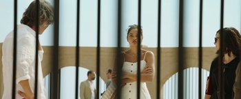 Movie still from “Greed” (2019), directed by Michael Winterbottom – A woman standing in front of a metal fence; Medium shot, Low angle