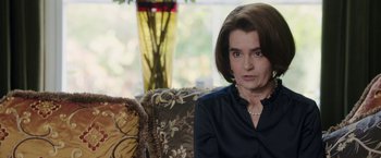 Movie still from “Greed” (2019), directed by Michael Winterbottom – A woman sitting on a couch in a living room; Close Up shot, Over the shoulder angle