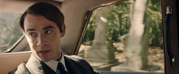 Movie still from “Greed” (2019), directed by Michael Winterbottom – A man in a suit and tie sitting in the back of a car; Close Up shot, Over the shoulder angle