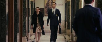 Movie still from “Greed” (2019), directed by Michael Winterbottom – A man and a woman are walking in a hallway; Medium shot, Low angle