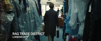 Movie still from “Greed” (2019), directed by Michael Winterbottom – A man in a suit and tie walking through a store; Wide shot, Over the shoulder angle