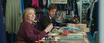 Movie still from “Greed” (2019), directed by Michael Winterbottom – A man and a woman sitting at a table in a room; Medium shot, Over the shoulder angle