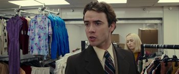 Movie still from “Greed” (2019), directed by Michael Winterbottom – A man in a suit and tie in a room; Close Up shot, Over the shoulder angle