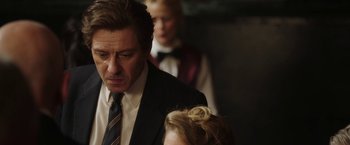 Movie still from “Greed” (2019), directed by Michael Winterbottom – A person wearing a suit and a tie; Close Up shot, Over the shoulder angle