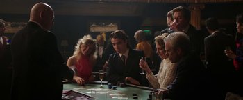 Movie still from “Greed” (2019), directed by Michael Winterbottom – A group of people sitting at a table with drinks; Medium shot, Over the shoulder angle