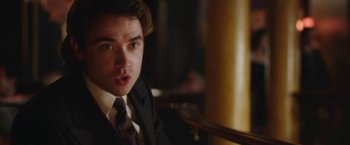 Movie still from “Greed” (2019), directed by Michael Winterbottom – A man in a suit and tie looking surprised; Close Up shot, Over the shoulder angle