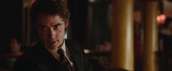 Movie still from “Greed” (2019), directed by Michael Winterbottom – A man in a suit and tie sitting at a table; Close Up shot, Over the shoulder angle