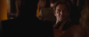 Movie still from “Greed” (2019), directed by Michael Winterbottom – A person wearing a suit and tie; Close Up shot, Over the shoulder angle