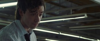 Movie still from “Greed” (2019), directed by Michael Winterbottom – A man in a tie looking at something in the distance; Close Up shot, Over the shoulder angle