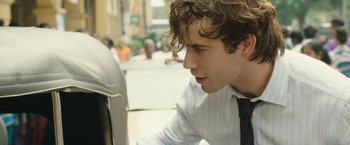 Movie still from “Greed” (2019), directed by Michael Winterbottom – A young man in a white dress shirt and a black tie; Close Up shot, Over the shoulder angle