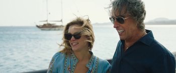 Movie still from “Greed” (2019), directed by Michael Winterbottom – A man and a woman wearing sunglasses next to a body of water; Close Up shot, High angle