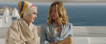 Movie still from “Greed” (2019), directed by Michael Winterbottom – Two women sitting next to each other near a body of water; Close Up shot, High angle