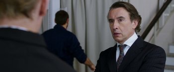 Movie still from “Greed” (2019), directed by Michael Winterbottom – A person wearing a suit and a tie; Close Up shot, Over the shoulder angle