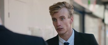 Movie still from “Greed” (2019), directed by Michael Winterbottom – A man in a suit and tie looking to his left; Close Up shot, Over the shoulder angle