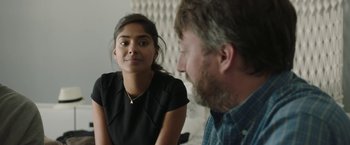 Movie still from “Greed” (2019), directed by Michael Winterbottom – A man and a woman sitting in front of each other in a room; Close Up shot, Over the shoulder angle