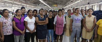 Movie still from “Greed” (2019), directed by Michael Winterbottom – A group of people standing together in a store; Medium shot, Low angle