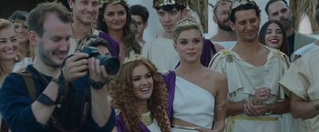 Movie still from “Greed” (2019), directed by Michael Winterbottom – A group of people dressed in ancient roman clothing; Close Up shot, Over the shoulder angle