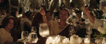 Movie still from “Greed” (2019), directed by Michael Winterbottom – A man pouring wine into a glass at a party; Medium shot, Low angle