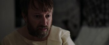 Movie still from “Greed” (2019), directed by Michael Winterbottom – A person with a beard; Close Up shot, Over the shoulder angle