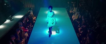Movie still from “Greed” (2019), directed by Michael Winterbottom – A woman in a white dress on a runway; Wide shot, Low angle