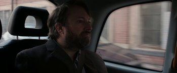 Movie still from “Greed” (2019), directed by Michael Winterbottom – A man with a goatee sitting in the back of a car; Close Up shot, Over the shoulder angle