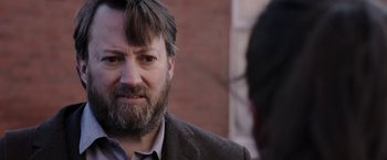 Movie still from “Greed” (2019), directed by Michael Winterbottom – A man with a goatee and beard talking to someone; Close Up shot, Over the shoulder angle