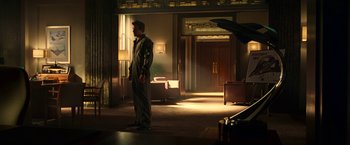 Movie still from “Green Lantern” (2011), directed by Martin Campbell – A man standing in a dimly - lit room with a suitcase; Wide shot, Low angle