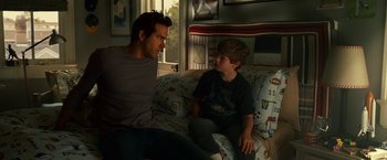 Movie still from “Green Lantern” (2011), directed by Martin Campbell – A man and a boy are sitting on a couch; Medium shot, Over the shoulder angle