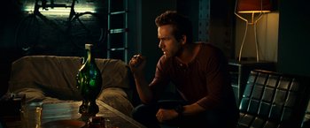 Movie still from “Green Lantern” (2011), directed by Martin Campbell – A man sitting on the ground in front of a green glass bottle; Medium shot, Low angle
