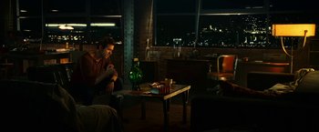 Movie still from “Green Lantern” (2011), directed by Martin Campbell – A man sitting on a couch in front of a table with drinks; Wide shot, High angle