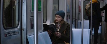 Movie still from “Greta” (2018), directed by Neil Jordan – A woman sitting on a train reading a book; Medium shot, Over the shoulder angle