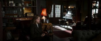 Movie still from “Greta” (2018), directed by Neil Jordan – A woman sitting in a chair in a room with a piano; Wide shot, High angle