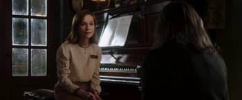 Movie still from “Greta” (2018), directed by Neil Jordan – A woman sitting in front of a piano talking to someone; Medium shot, Over the shoulder angle