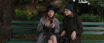 Movie still from “Greta” (2018), directed by Neil Jordan – Two women sitting on a bench looking at a cell phone; Medium shot, Over the shoulder angle