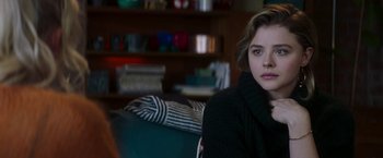 Movie still from “Greta” (2018), directed by Neil Jordan – A woman sitting on a couch in front of a bookshelf; Close Up shot, Over the shoulder angle