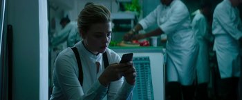 Movie still from “Greta” (2018), directed by Neil Jordan – A woman is looking at her cell phone in a kitchen; Medium shot, Low angle