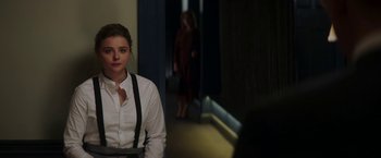 Movie still from “Greta” (2018), directed by Neil Jordan – A woman in white shirt and black suspenders standing in hallway; Medium shot, Over the shoulder angle