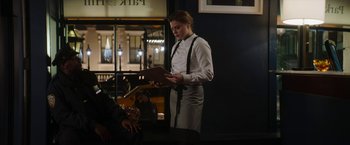 Movie still from “Greta” (2018), directed by Neil Jordan – A woman standing in front of a table holding a book; Medium shot, Over the shoulder angle