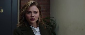 Movie still from “Greta” (2018), directed by Neil Jordan – A young woman in a green jacket looking at the camera; Close Up shot, Over the shoulder angle