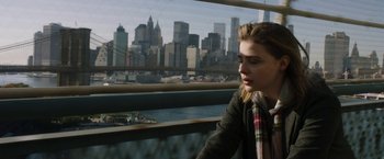 Movie still from “Greta” (2018), directed by Neil Jordan – A woman sitting in front of a window with a view of a city; Medium shot, High angle