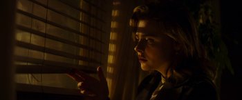 Movie still from “Greta” (2018), directed by Neil Jordan – A woman sitting in front of a window with her hand up to her face; Close Up shot, Low angle