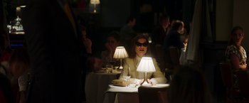 Movie still from “Greta” (2018), directed by Neil Jordan – A woman sitting at a table with two lamps on top of it; Medium shot, Over the shoulder angle