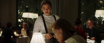 Movie still from “Greta” (2018), directed by Neil Jordan – A woman standing next to a lamp in a room; Medium shot, Over the shoulder angle