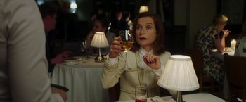 Movie still from “Greta” (2018), directed by Neil Jordan – A woman sitting at a table holding a glass of wine; Medium shot, Over the shoulder angle