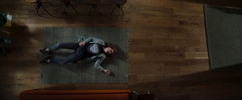 Movie still from “Greta” (2018), directed by Neil Jordan – A woman laying on the floor holding a remote control; Wide shot, Overhead angle