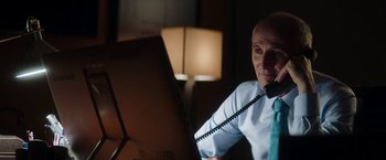 Movie still from “Greta” (2018), directed by Neil Jordan – A man sitting in front of a computer with a phone to his ear; Medium shot, Over the shoulder angle