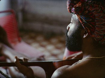 Movie still from “Guava Island” (2019), directed by Hiro Murai – A man with a beard is holding a knife in his hand; Close Up shot, Over the shoulder angle