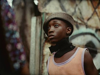 Movie still from “Guava Island” (2019), directed by Hiro Murai – A young man wearing a hat and a neck scarf; Close Up shot, Low angle