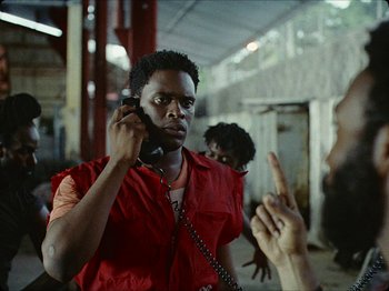 Movie still from “Guava Island” (2019), directed by Hiro Murai – A man holding a cell phone up to his ear; Medium shot, Over the shoulder angle