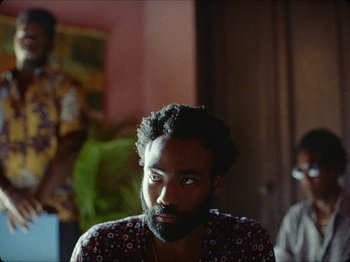 Movie still from “Guava Island” (2019), directed by Hiro Murai – A person with a beard looking at the camera; Close Up shot, Over the shoulder angle